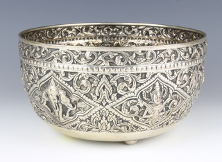 A late 19th Century Indian repousse silver chased bowl decorated with panels of deities and elephants on a ground of formal scrolling leaves and flowers, raised on bun fee, the underside engraved with a figure of a deity, 590 grams, stamped Hua Chang Bangkok, 23 cm