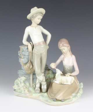 A Lladro group of a standing youth and a kneeling girl feeding a lamb 27cm 