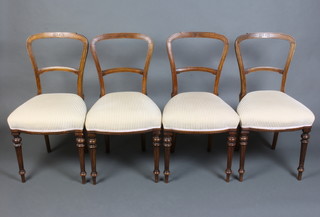 A set of 4 Victorian spoon back dining chairs with carved mid rails, the seats upholstered in striped material raised on turned and fluted supports