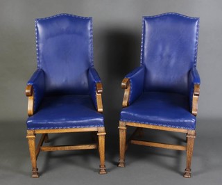 A pair of Edwardian oak Masonic style throne chairs raised on square tapered supports ending in spade feet united by an H framed stretcher and upholstered in garter blue rexine
