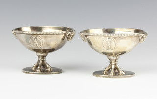 A pair of George III oval silver boat shaped table salts decorated with rams heads and classical figures, raised on hoof feet on oval bases 7cm, 260 grams