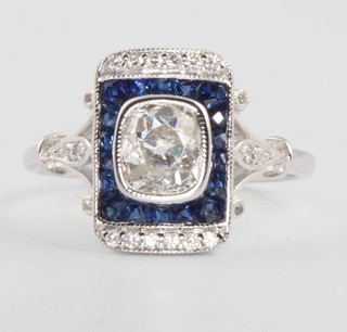An 18ct white gold sapphire and diamond Art Deco style ring, the centre mine cut diamond approx 0.9ct surrounded by sapphires and diamonds, size N 