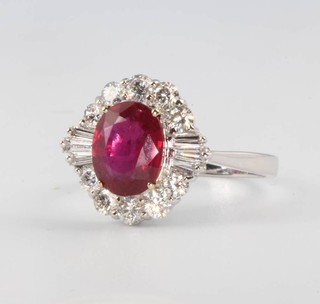 An 18ct white gold oval, ruby and diamond cluster ring, the treated centre stone 2.14ct, surrounded by brilliant cut diamonds 0.69ct and tapered  baguette cut diamonds 0.15ct, size O 