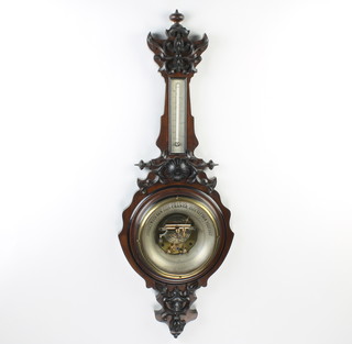 An Edwardian aneroid barometer and thermometer with concave silvered dial, contained in a carved walnut wheel case 