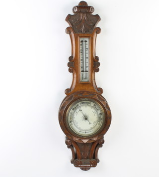 An Edwardian aneroid barometer and thermometer with porcelain dial contained in a carved oak wheel case 