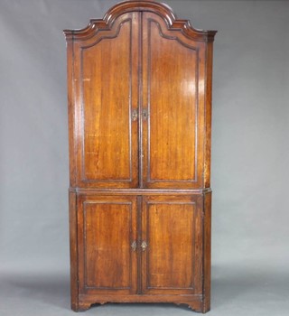 An 18th/19th Century Continental oak double corner cabinet the upper section with moulded cornice, fitted shelves enclosed by arched panelled doors the base enclosed by panelled doors, raised on bracket feet 225cm h x 103cm w 