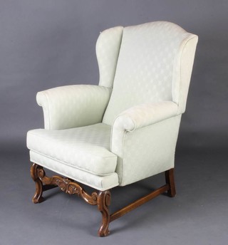 A Georgian style winged armchair upholstered in green material, raised on shaped supports
