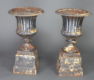 A pair of Victorian style circular cast iron urns with demi-fluted decoration raised on square bases 69cm x 39cm 