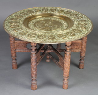 A Burmese embossed brass tray table raised on a carved hardwood folding stand 50cm x 78cm diam. 
