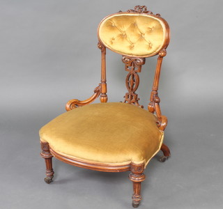 A Victorian carved walnut show frame nursing chair upholstered in mustard coloured buttoned material, raised on turned and fluted supports 