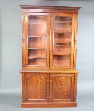 A Victorian carved walnut bookcase on cabinet the upper section with moulded cornice, the interior fitted adjustable shelves enclosed by arched glazed panelled doors, the base fitted a double cupboard enclosed by panelled doors 227cm h x 135cm w x 52cm d 