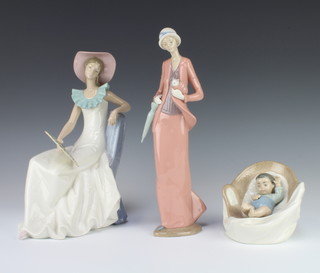 A Nao figure of a seated lady holding a fan 26cm, ditto lady with a cat in her jacket 30cm and a sleeping child in a bassinet 10cm