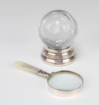 A cut glass ball on a silver stand together with a magnifying glass with a mother of pearl handle