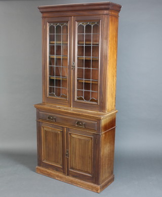 An Art Nouveau mahogany display cabinet with moulded cornice, fitted adjustable shelves enclosed by lead glazed panelled doors, the base fitted a drawer above a double cupboard enclosed by panelled doors, raised on a platform base 207cm h x 95cm w x 36cm d 