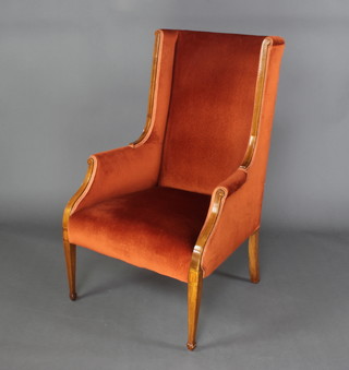 An Edwardian Art Nouveau inlaid mahogany wing back armchair upholstered in orange material, raised on square tapered supports 