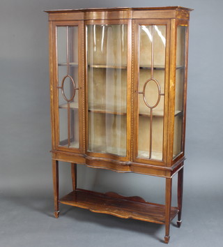 An Edwardian inlaid mahogany display cabinet of serpentine outline, fitted shelves enclosed by astragal glazed panelled doors, the base with under tier 178cm h x 114cm w x 40cm d 