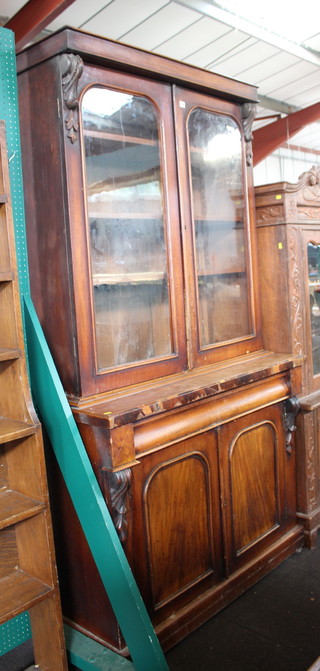 A Victorian mahogany bookcase on cabinet with moulded cornice, the upper section enclosed by arched glazed panelled doors, the base fitted a secret drawer above a double cupboard 218cm h x 120cm w x 54cm d (some veneers missing in places) 