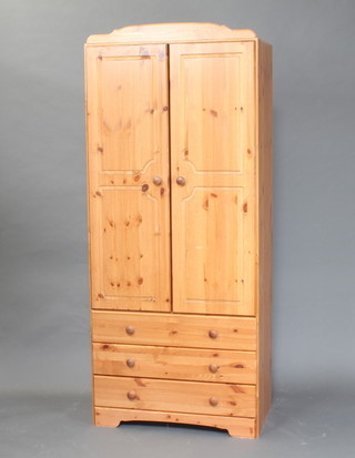 A pine wardrobe the upper section fitted a cupboard enclosed by a panelled door, the base fitted 3 long drawers with tore handles 196cm h x 82cm w x 49c, 