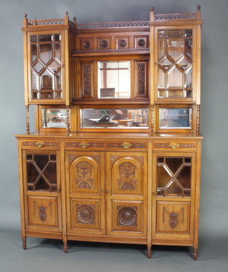 James Shoolbred, an Arts and Crafts carved walnut chiffonier sideboard, the raised inverted breakfront back with pierced gallery, the centre section fitted a shelf with pierced gallery above a square bevelled plate mirror flanked by a pair of cupboards enclosed by astragal bevelled glazed panelled doors, the base fitted triple mirrors above 1 long and 2 short drawers above a further cupboard enclosed by carved panelled doors, raised on turned feet 205cm h x 152cm w x 44cm d 