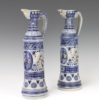 A pair of German blue glazed jugs with mask spouts and scroll handles decorated with mythical beasts and crests 36cm 