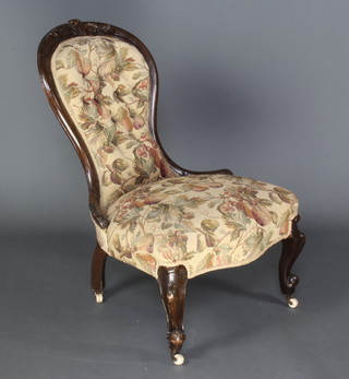 A Victorian carved mahogany nursing chair upholstered in brown material, raised on cabriole supports 