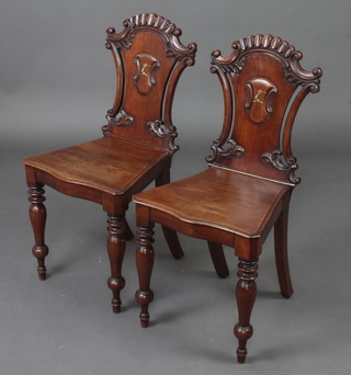 A pair of Victorian mahogany hall chairs with armorial decoration, raised on turned legs 