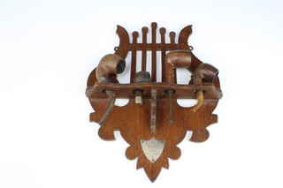 An Edwardian oak pierced wall mounting pipe rack in the form of a lyre 32cm x 24cm together with a pipe with silver band and 3 others 