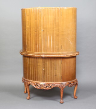 An Art Deco walnut D shaped cocktail cabinet, fitted peach coloured mirrored glass panels, the base with brushing slide above a cupboard enclosed by a panelled door with carved and pierced apron, on cabriole supports 172cm h x 108cm w x 57cm d 