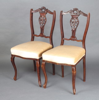 A pair of Edwardian carved and pierced walnut slat back dining chairs with overstuffed sets on cabriole supports 