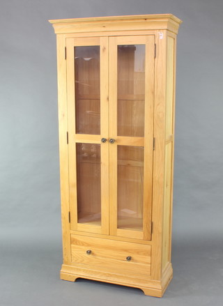 A light hardwood cabinet, fitted shelves enclosed by glazed panelled doors, the base fitted a drawer, raised on bracket feet 192cm h x 85cm w 