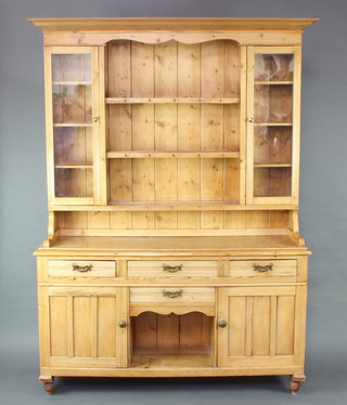 A Victorian style pine dresser with moulded cornice, the raised back fitted shelves and cupboards enclosed by glazed panelled doors, the base fitted an arrangement of 3 drawers above a recess, flanked by cupboards, raised on turned bun feet 218cm h x 155cm w x 42cm d  