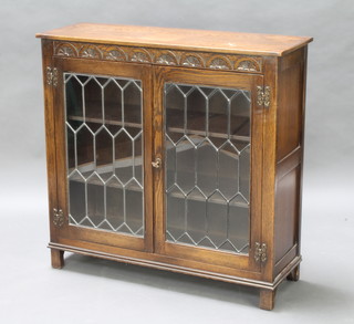 A carved oak bookcase/display cabinet fitted a shelf enclosed by  lead glazed panelled doors, raised on block supports 92cm h x 94cm w x 32cm d 

