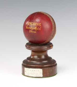A Spalding 5 1/2 oz cricket ball raised on a turned wooden plinth marked 56 K.B.A.CM 1936 bowling prize 13cm 