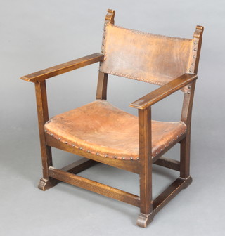 A 1930's oak framed open arm chair upholstered in leather, raised on square supports 
