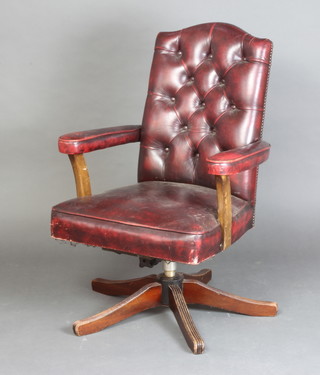 An open arm revolving office chair upholstered in red buttoned leather 
