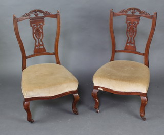 A pair of Edwardian pierced and carved walnut nursing chairs, the over stuffed seats of serpentine outline raised on cabriole supports 