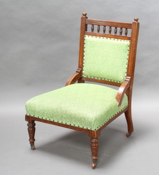 An Edwardian oak nursing chair with bobbin turned decoration, the seat and back upholstered in green material, on turned supports 