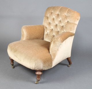 A Victorian armchair upholstered in buttoned light brown fabric, raised on turned supports 