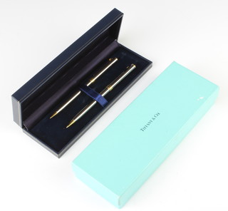 A Tiffany & Co steel cased and gilt metal mounted propelling pencil and ballpoint pen in a fitted box
