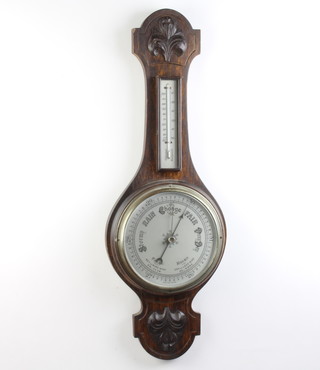 A 1930's aneroid barometer and thermometer with 19cm silvered dial contained in a carved oak wheel case 
