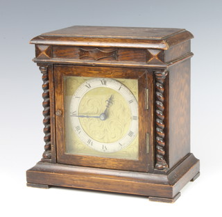 A 1930's timepiece with gilt dial and silvered chapter ring, contained in a carved oak case with spiral turned columns to the sides 