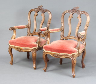 A pair of French heavily carved walnut tulip back open arm chairs with overstuffed upholstered seats, raised on cabriole supports