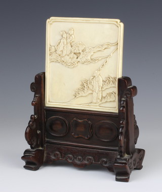An early 20th Century small ivory table screen, almost square and carved in relief with a fisherman on a riverbank amazed at an immortal and maiden in the clouds, 9.8cm, with original carved hardwood stand, combined height 18cm   
