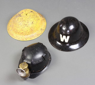 A fire watchers black painted helmet marked W (no liner), a yellow painted steel helmet (no liner and corrosion holes) together with a minors safety helmet and lamp 