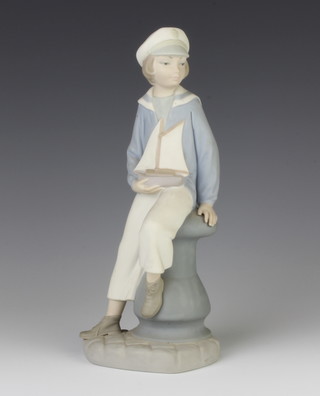 A Lladro matt figure of a boy sailor holding a toy boat, sitting on a capstan 23cm 