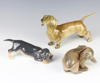 A Continental figure of a standing Dachshund 23cm, a Royal Copenhagen figure of a puppy 17cm and a ditto of a puppy 11cm 