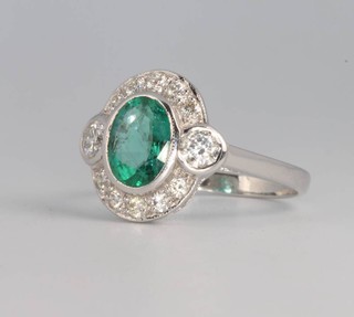 An 18ct white gold oval emerald and diamond cluster ring, the centre stone approx. 1.5ct surrounded by brilliant cut diamonds approx. 0.75ct, size N 