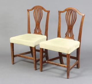 A pair of Georgian oak Hepplewhite style camel back dining chairs with pierced vase shaped slat backs and overstuffed seats, raised on square tapered supports with H framed stretcher 