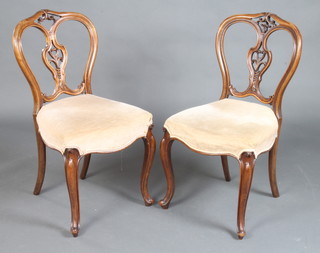 A pair of Victorian carved mahogany spoon back dining chairs with overstuffed seats, carved and pierced splat backs, raised on French cabriole supports 