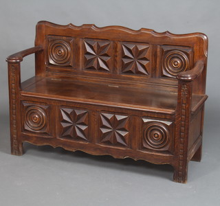 A 1920's carved oak settle with panelled back, the seat with hinged lid 84cm h x 182cm w x 41cm d 